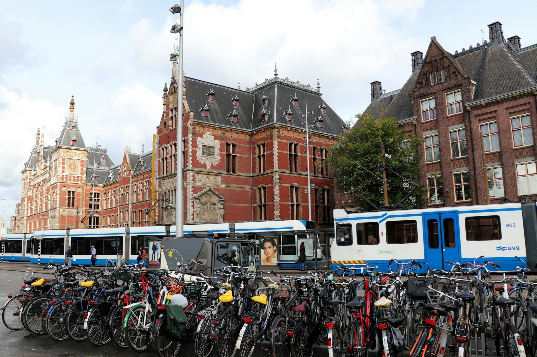 Estación de Amsterdam Centraal con bicicletas aparcadas en frente y tranvías azules y blancos pasando, ilustrando los principales modos de transporte urbano juntos.