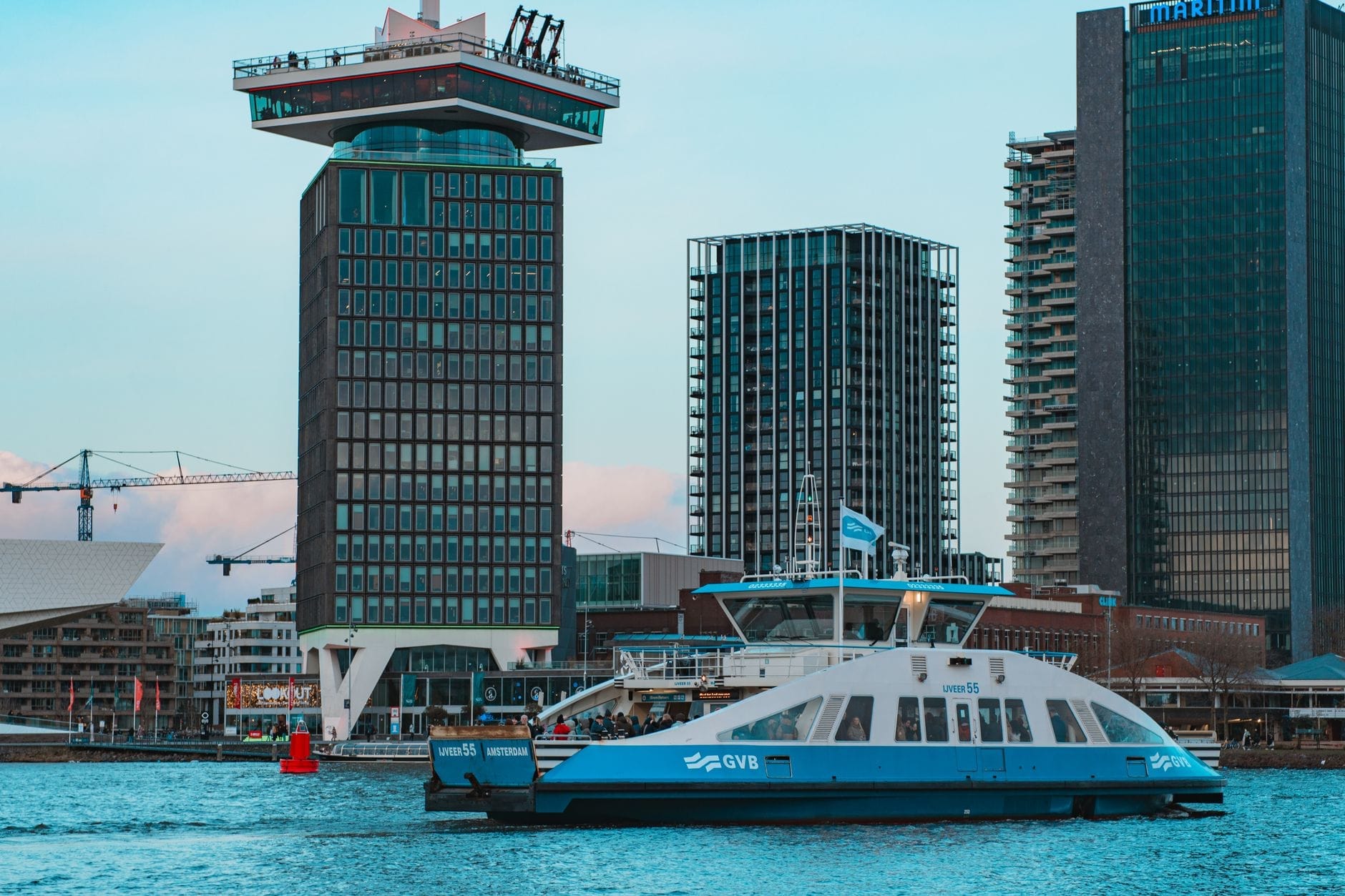 Transbordador GVB cruzando el río IJ en Ámsterdam con la A'DAM Tower y edificios modernos al fondo.