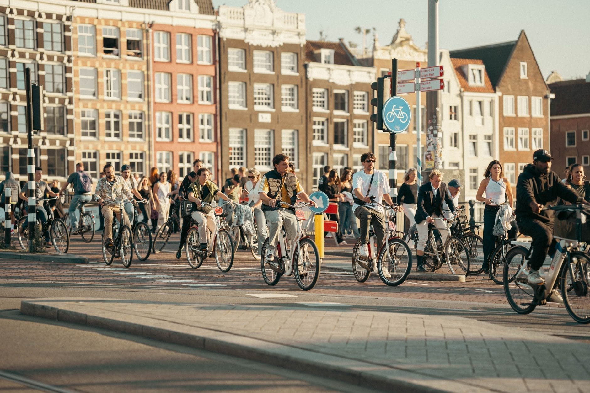 Gran grupo de personas en bicicleta en un carril exclusivo en Ámsterdam con edificios históricos al fondo.