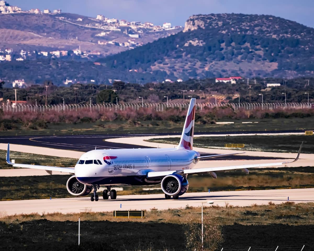 Verkehrsflugzeug rollt auf einer Startbahn des Internationalen Flughafens Athen mit Hügeln und Gebäuden im Hintergrund