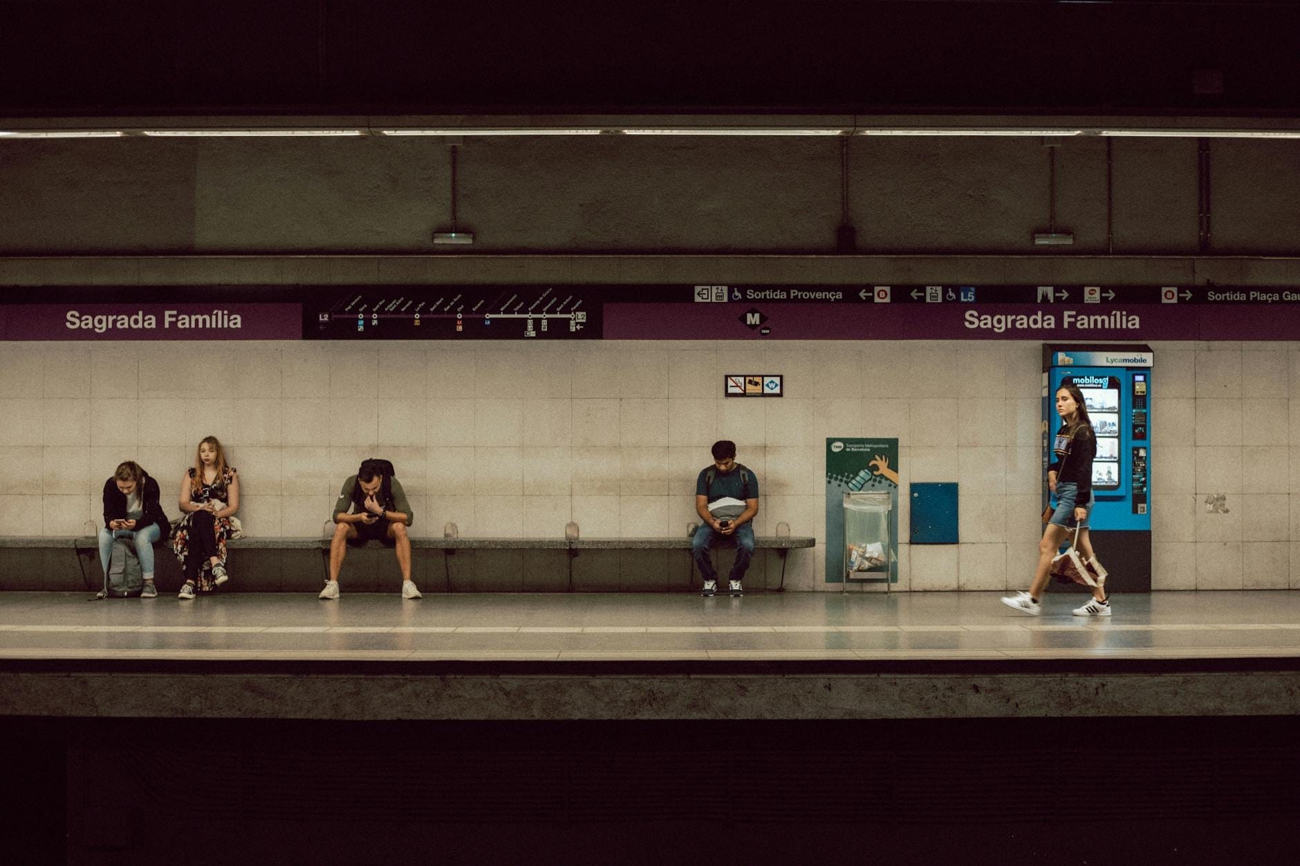 Interior of Sagrada Família metro station in Barcelona with people waiting on the platform and visible station signage.