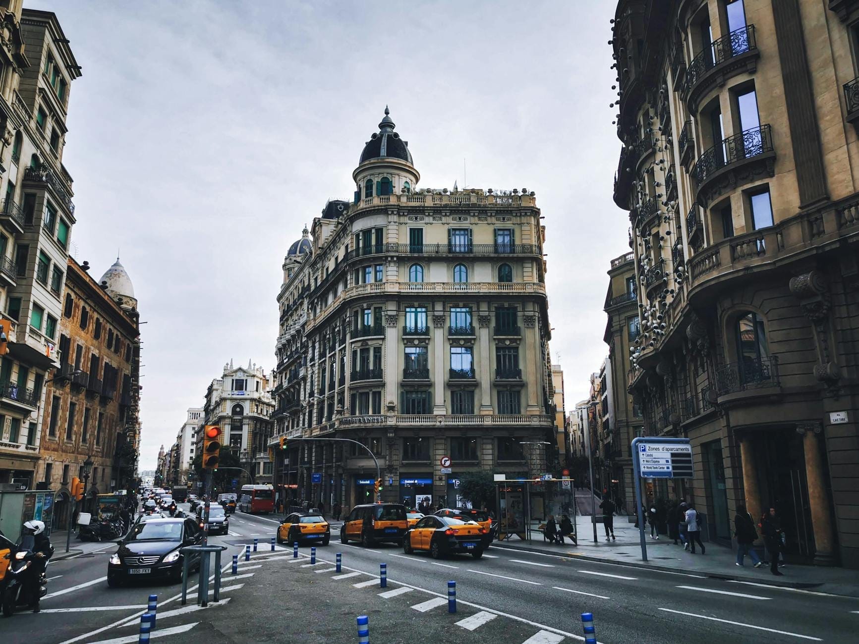 Street scene in Barcelona with several black and yellow taxis waiting by ornate historic buildings and bustling pedestrians.