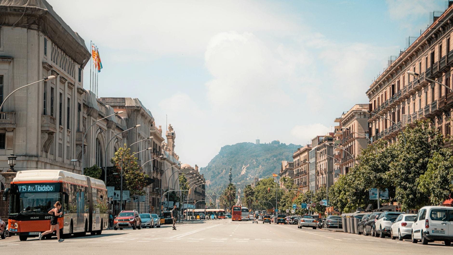Wide Barcelona street scene with city buses, taxis, and cars, flanked by historic buildings and distant hills, showcasing various urban transport options.