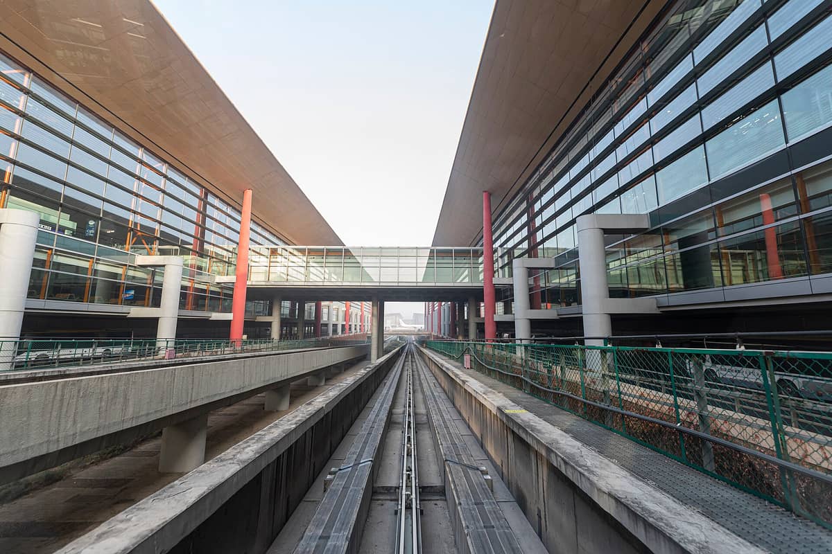 Moderne Außenansicht des Terminalgebäudes des Beijing Capital International Airport, mit einer Bahnlinie, die zum Eingang führt.