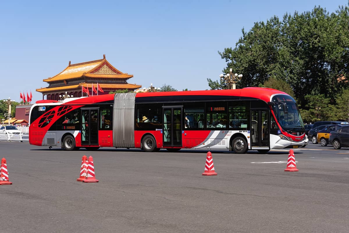 Moderner roter Stadtbus aus Beijing fährt vor dem historischen Tiananmen-Tor vor blauem Himmel.