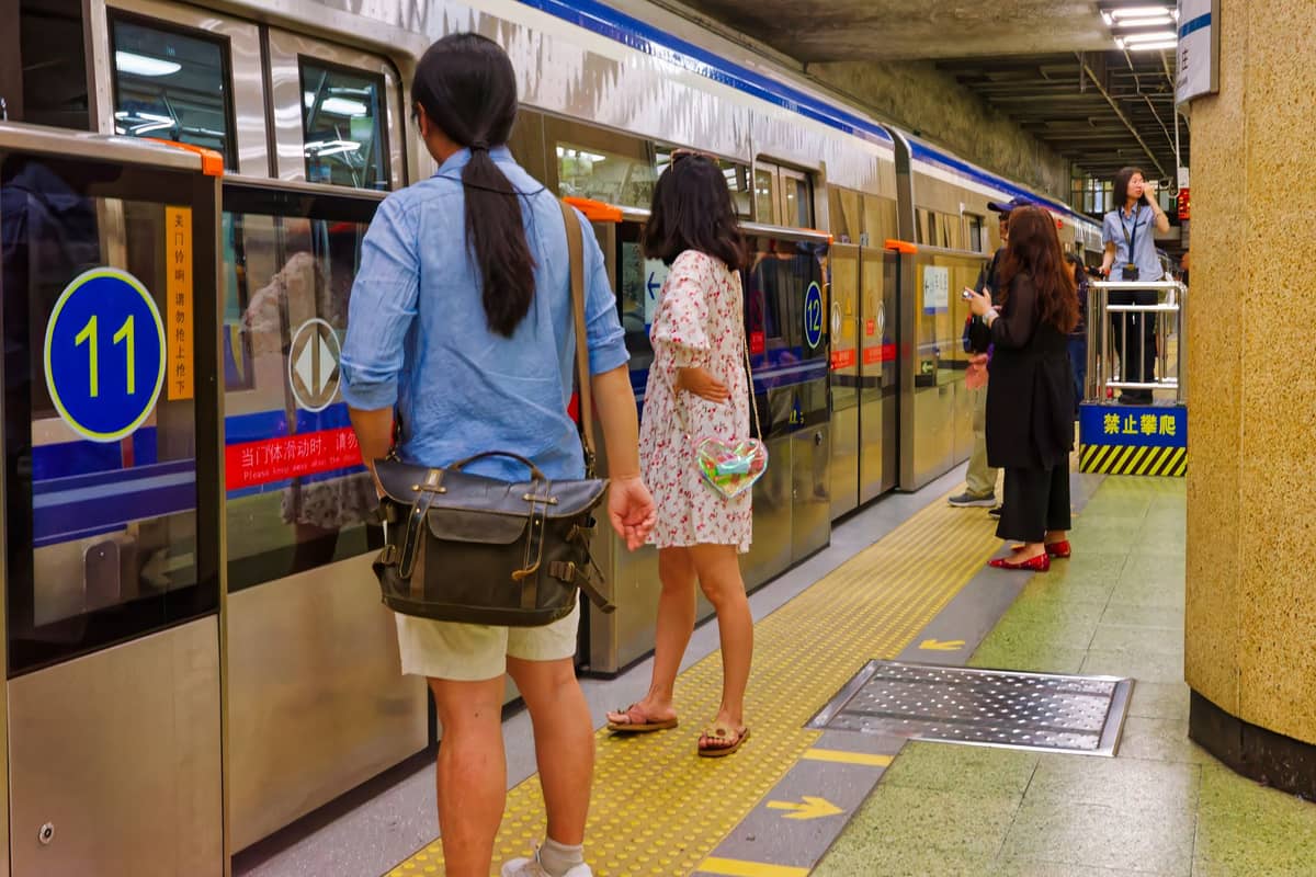 Menschen warten auf einen Pekinger U-Bahn-Zug in einer unterirdischen Station, gut sichtbare Linien- und Bahnsteighinweise im Hintergrund.