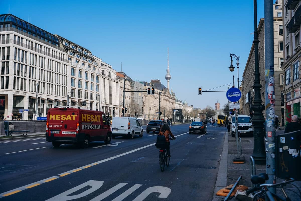 Stadtstraße in Berlin mit Radfahrer auf dem Radweg, Autos und dem Berliner Fernsehturm unter blauem Himmel.