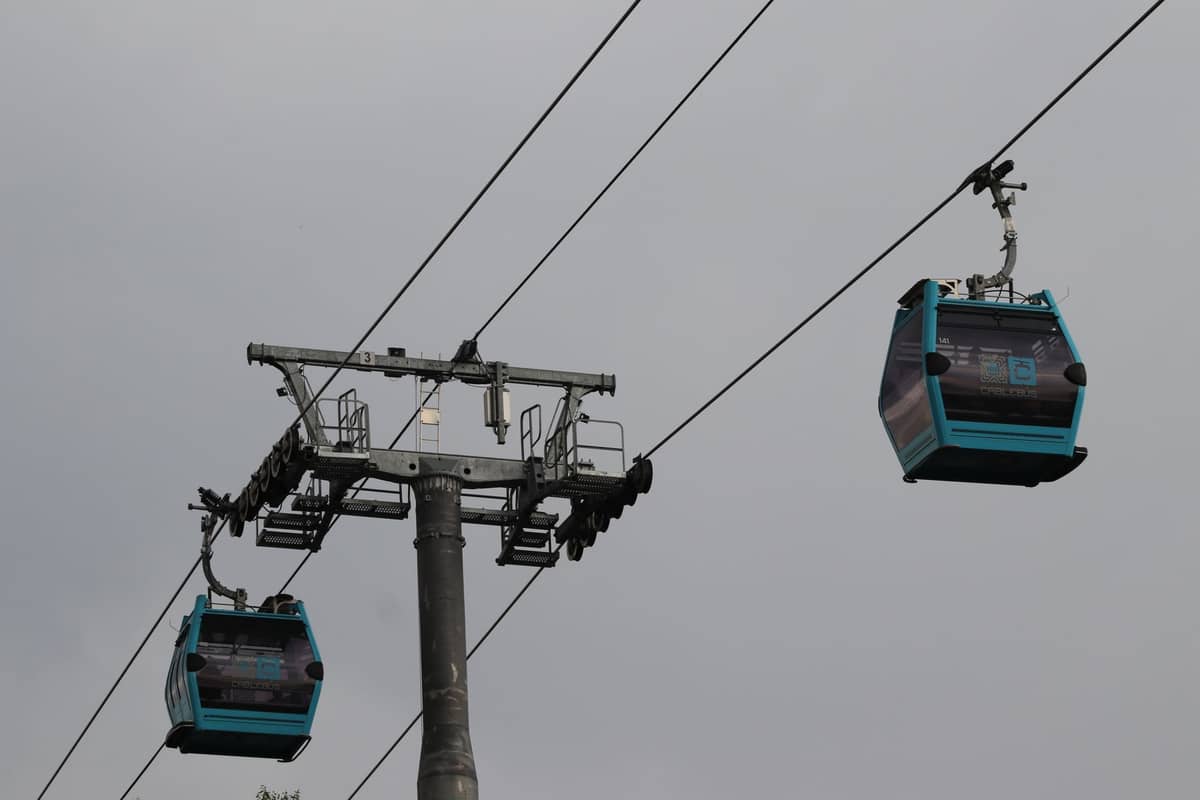 Three blue TransMiCable gondola cars suspended on cables with a gray sky in the background, showing Bogotá’s cable car system.