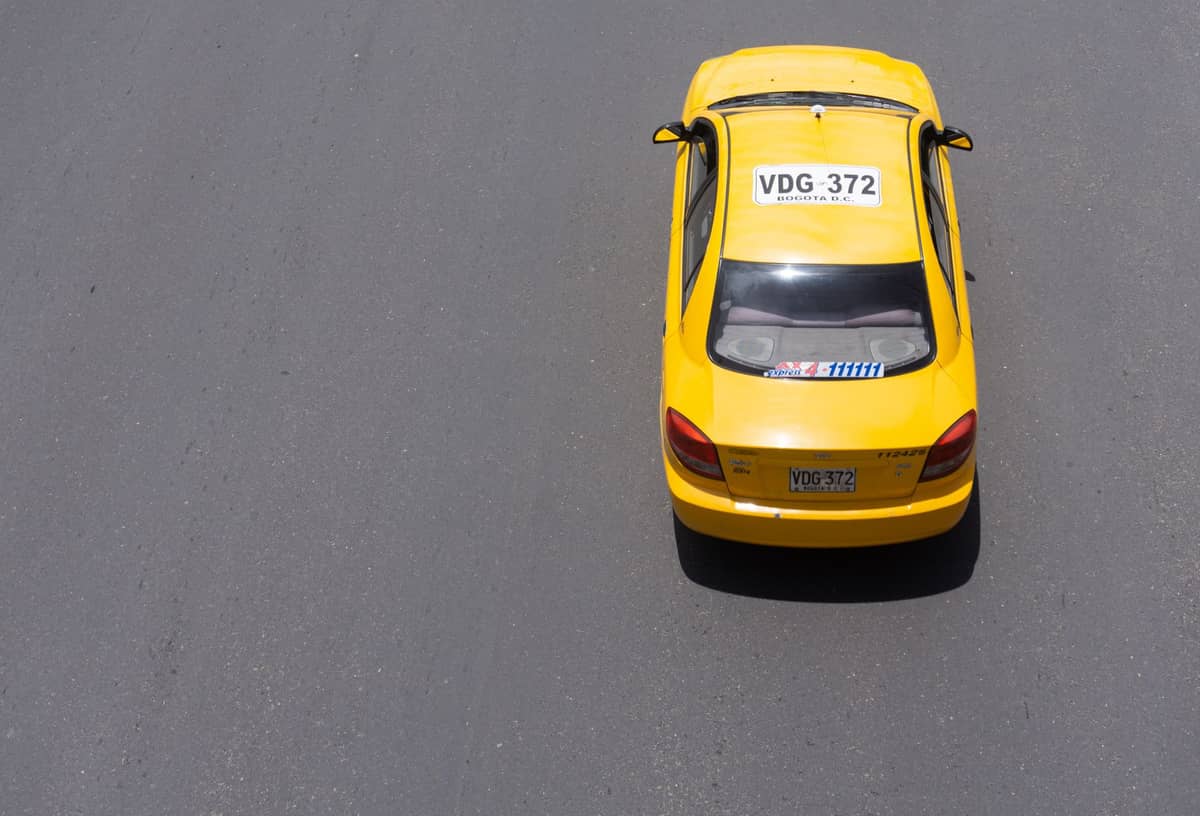 Yellow taxi drives on a city street in Bogotá, Colombia, viewed from above with license plate visible.