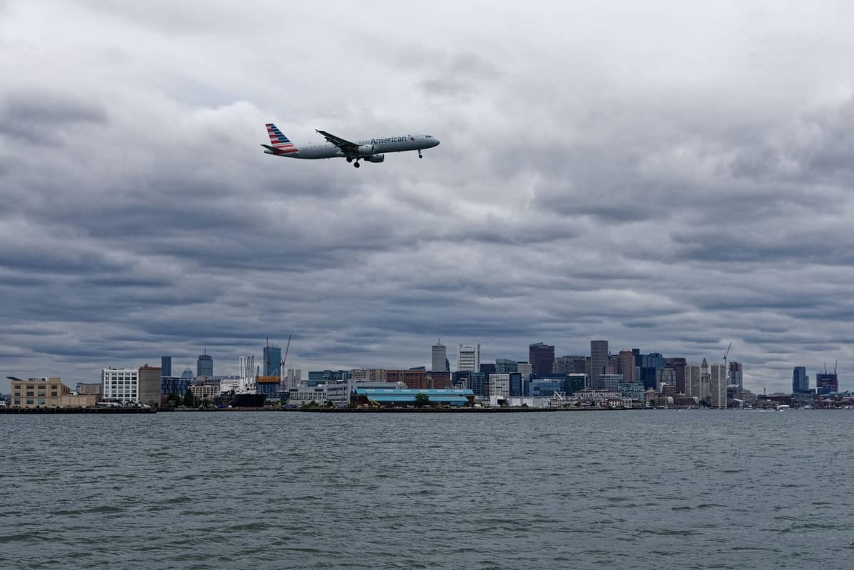 Flugzeug landet über Boston Harbor mit der Skyline von Boston im Hintergrund an einem bewölkten Tag.
