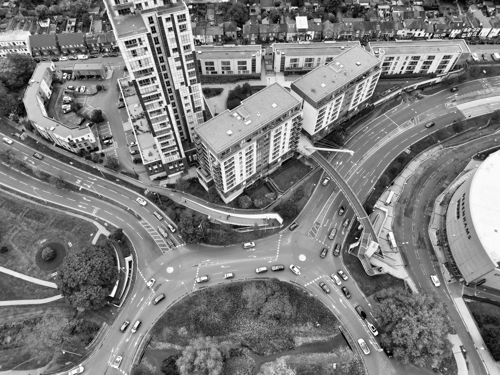 Schwarz-Weiß-Luftaufnahme eines komplexen Straßennetzes und moderner Gebäude mit mehreren Fahrspuren, Kreisverkehren und Straßenverkehr in einem städtischen Gebiet.