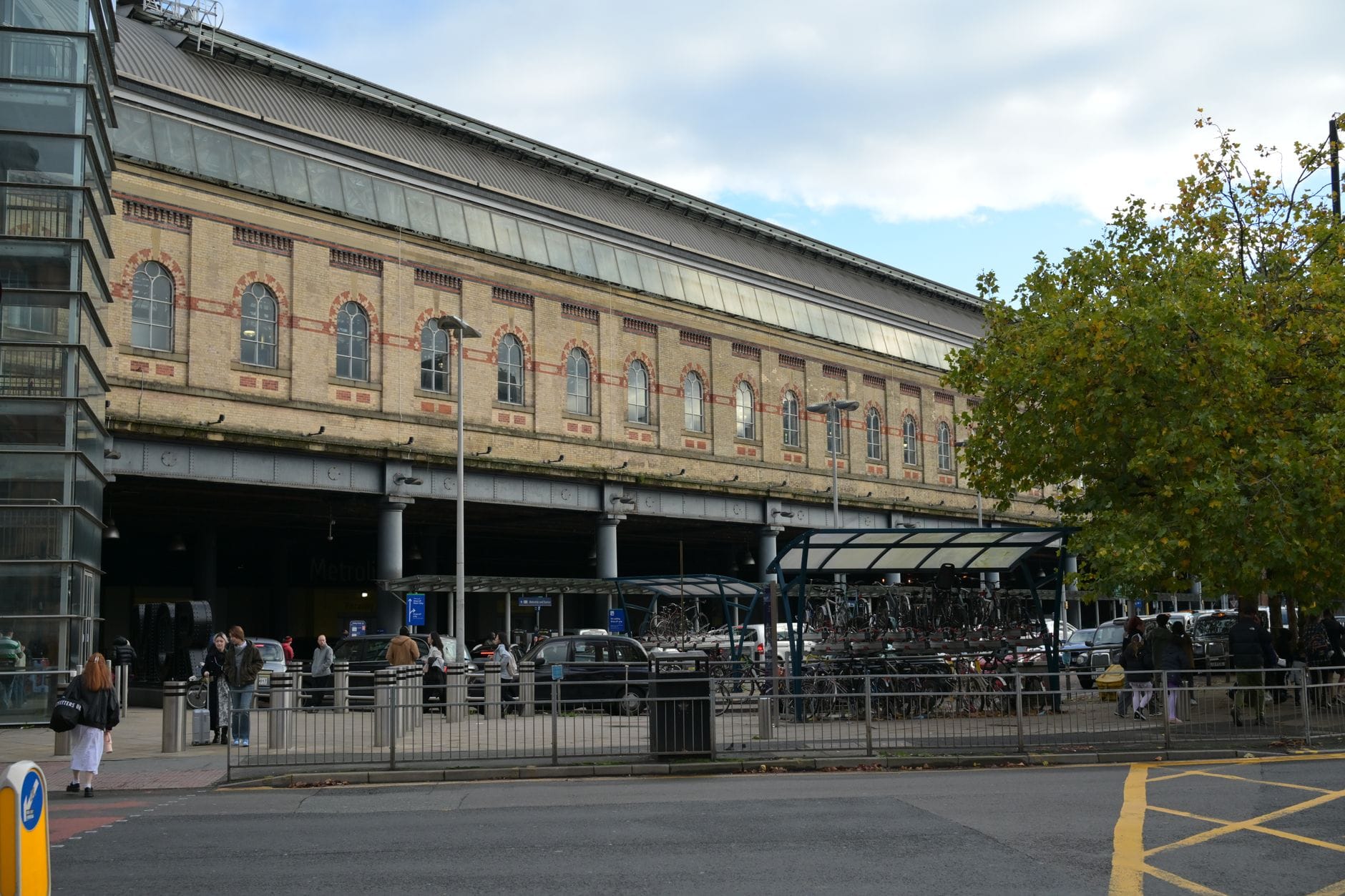 Außenansicht des Bahnhofs Brighton mit Menschen draußen und sichtbaren Fahrradstellplätzen vor dem historischen Backsteingebäude.