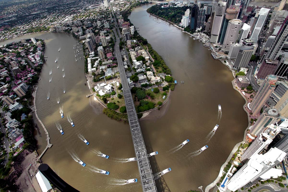 Aerial view of Brisbane River with multiple CityCat ferries traveling under Story Bridge and past city skyscrapers.