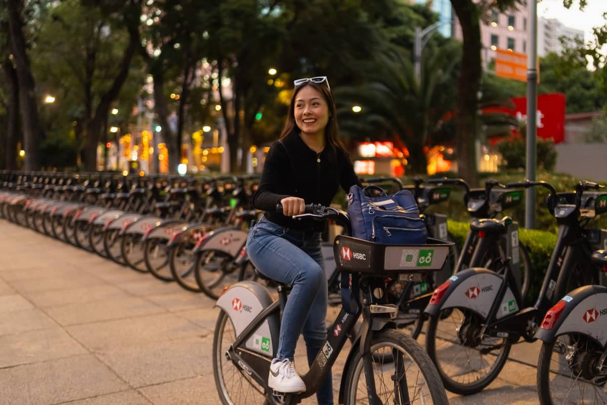 ผู้หญิงขี่จักรยาน Ecobici ในบัวโนสไอเรส โดยมีแถวจักรยานสาธารณะที่เหมือนกันและอาคารในเมืองเป็นฉากหลัง