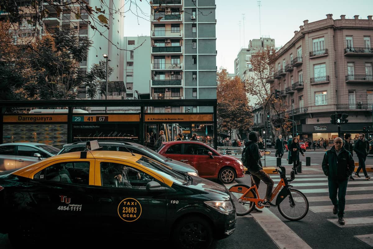 แท็กซี่สีเหลืองและดำของ Buenos Aires จอดรอที่สี่แยกในเมือง โดยมีคนเดินถนนกำลังข้ามถนนและอาคารอพาร์ตเมนต์ในเมืองเป็นฉากหลัง