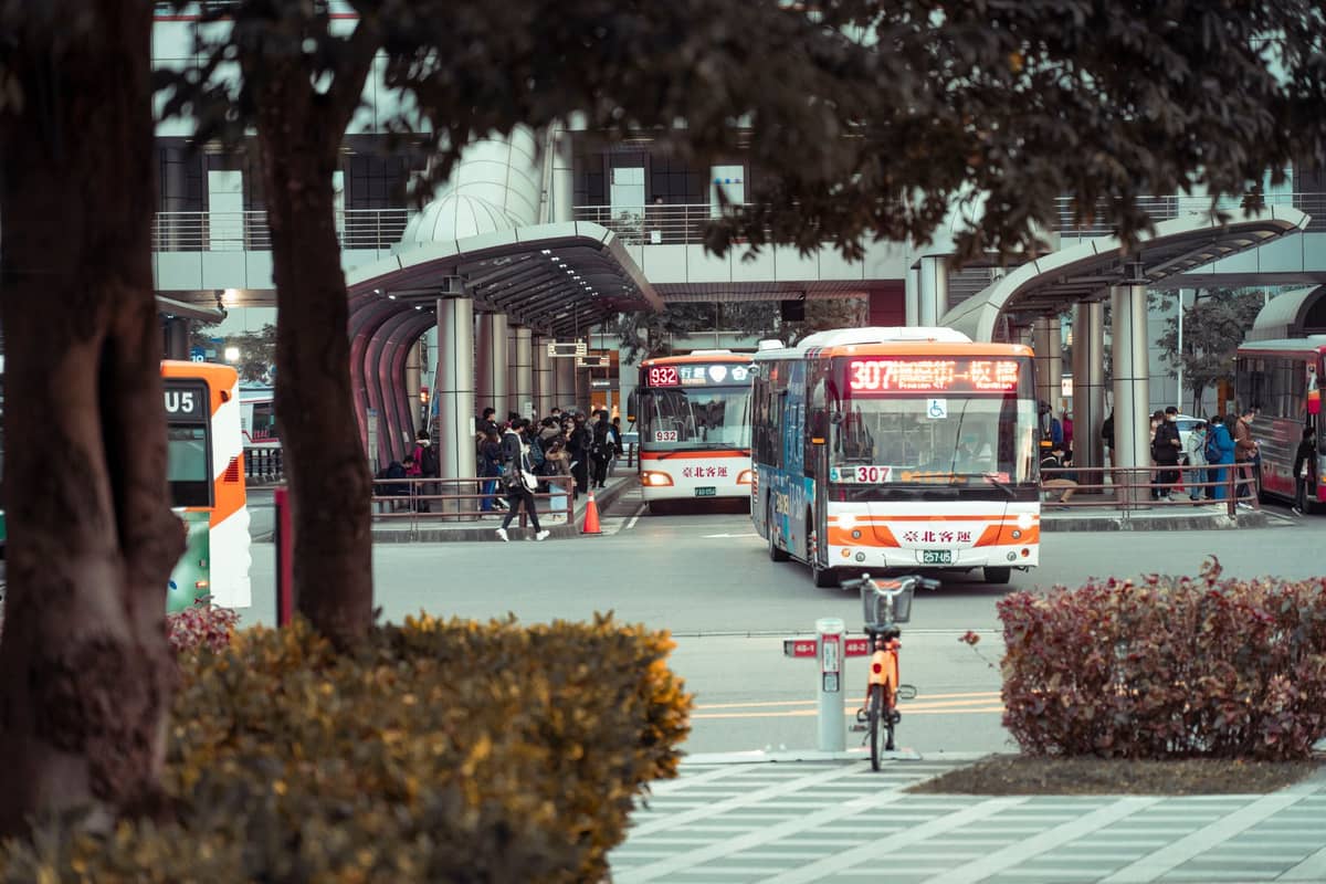 Varios autobuses urbanos y una bicicleta compartida en una moderna estación de autobuses en Chengdu con personas esperando para abordar.