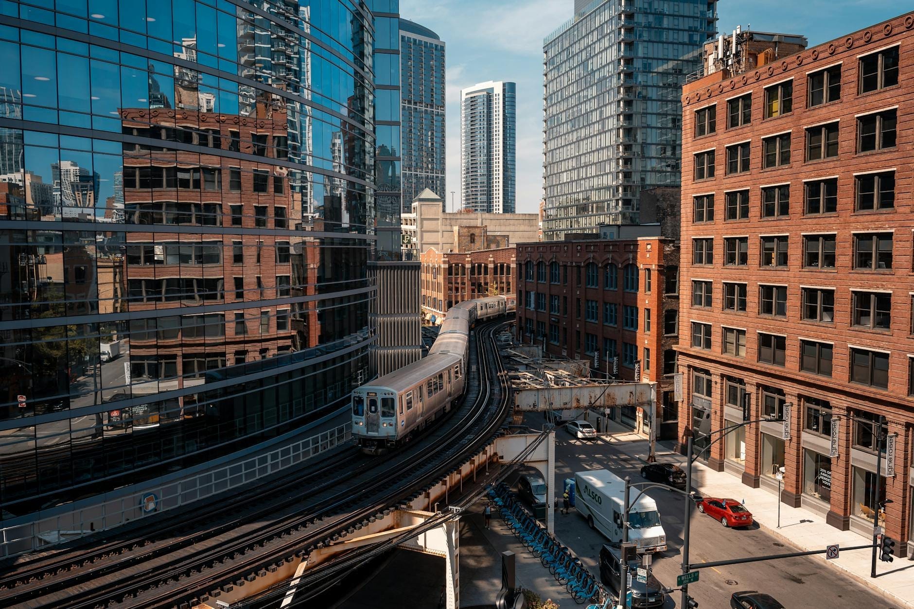 Um trem 'L' de Chicago faz uma curva entre os arranha-céus do centro em trilhos elevados, mostrando a arquitetura urbana, as ruas movimentadas e o icônico transporte público em um dia de céu limpo.