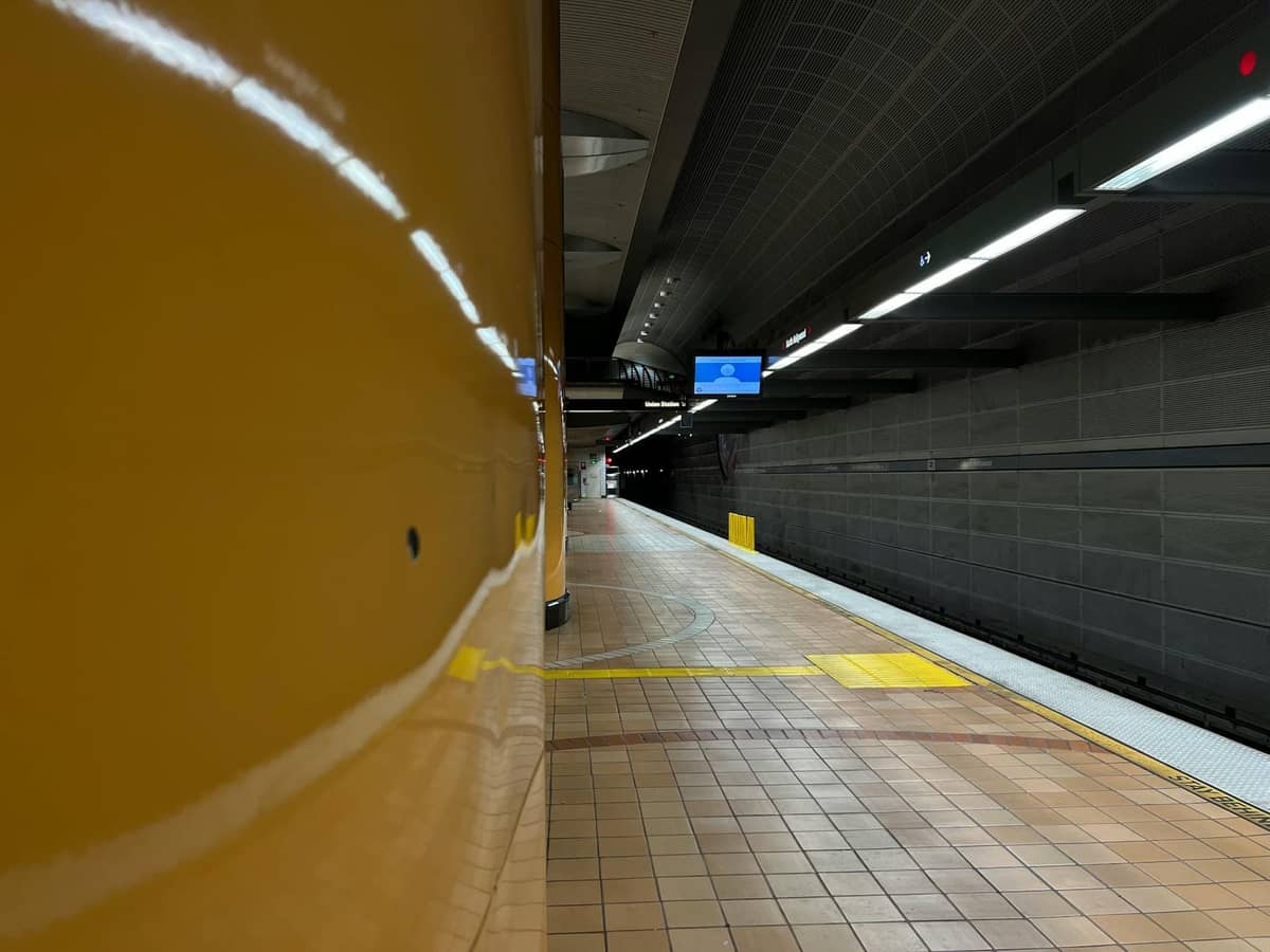 Wide view of a clean CTA 'L' train platform with yellow columns and signs, suggesting a Chicago transit station, possibly the Orange Line.