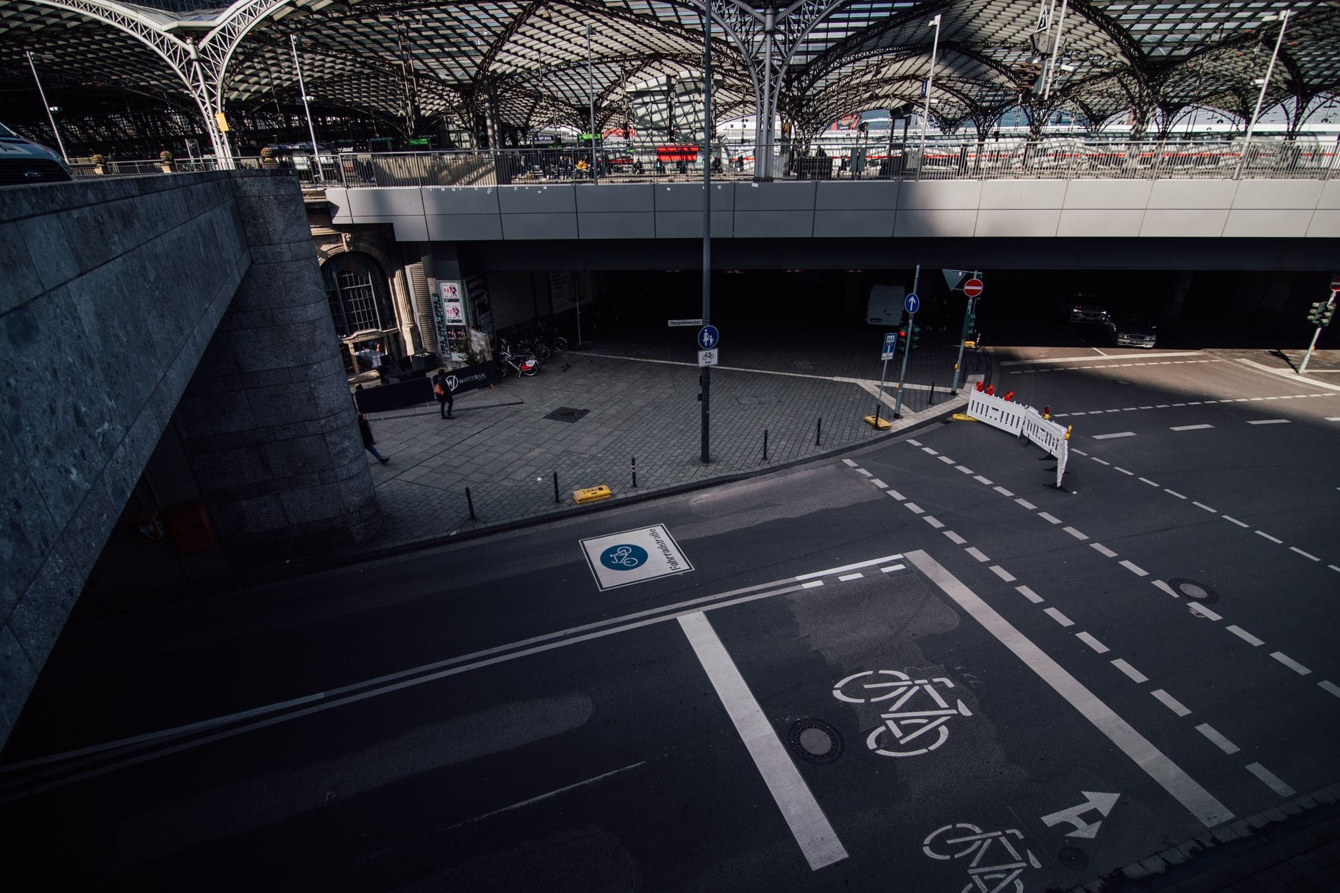 เครื่องหมายช่องทางจักรยานบนถนนใกล้ Cologne Hauptbahnhof พร้อมซุ้มเหล็กอันเป็นสัญลักษณ์ของสถานีที่มองเห็นได้ด้านบน