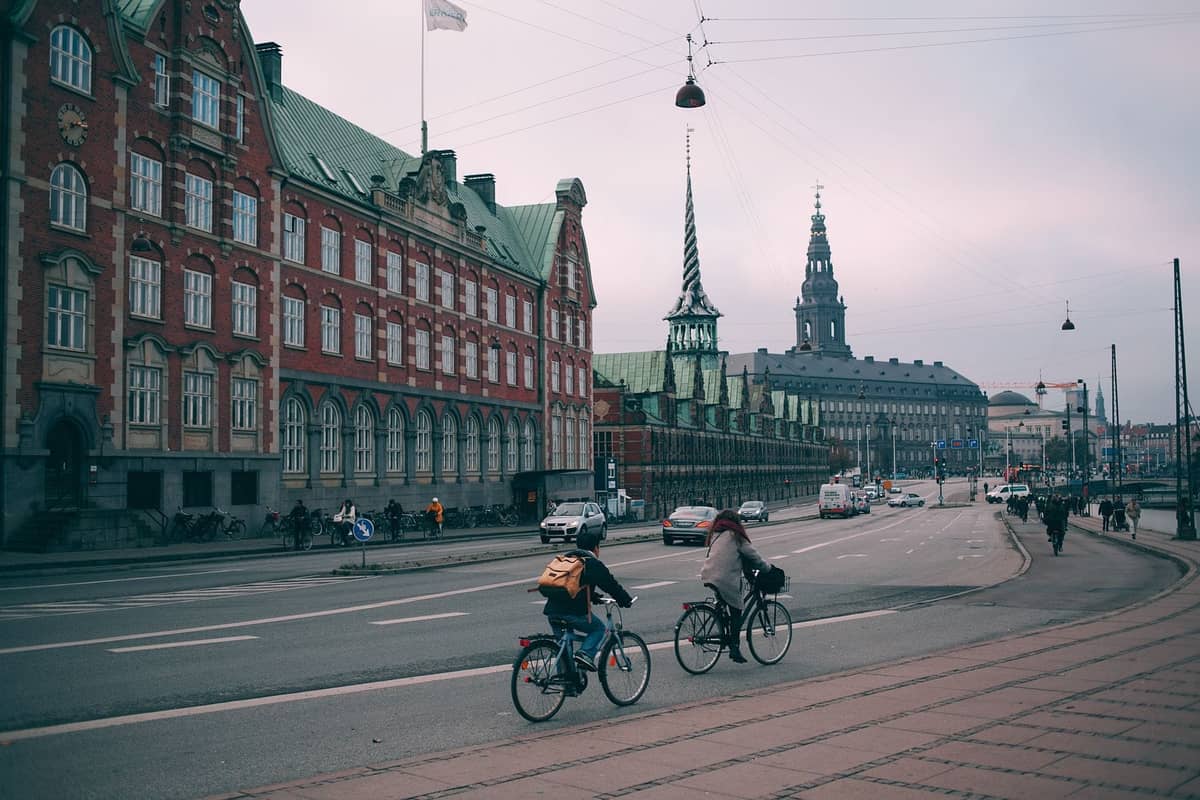 Radfahrer auf einer Straße in Kopenhagen mit historischen Gebäuden und dem sichtbaren Turm der Børsen, die das Alltagsleben der Stadt zeigen.