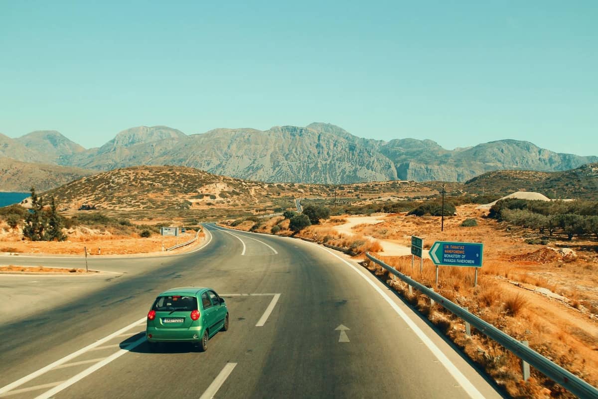 Auto che percorre un'autostrada attraverso un paesaggio secco e montuoso con segnali stradali greci e le montagne di Creta sullo sfondo