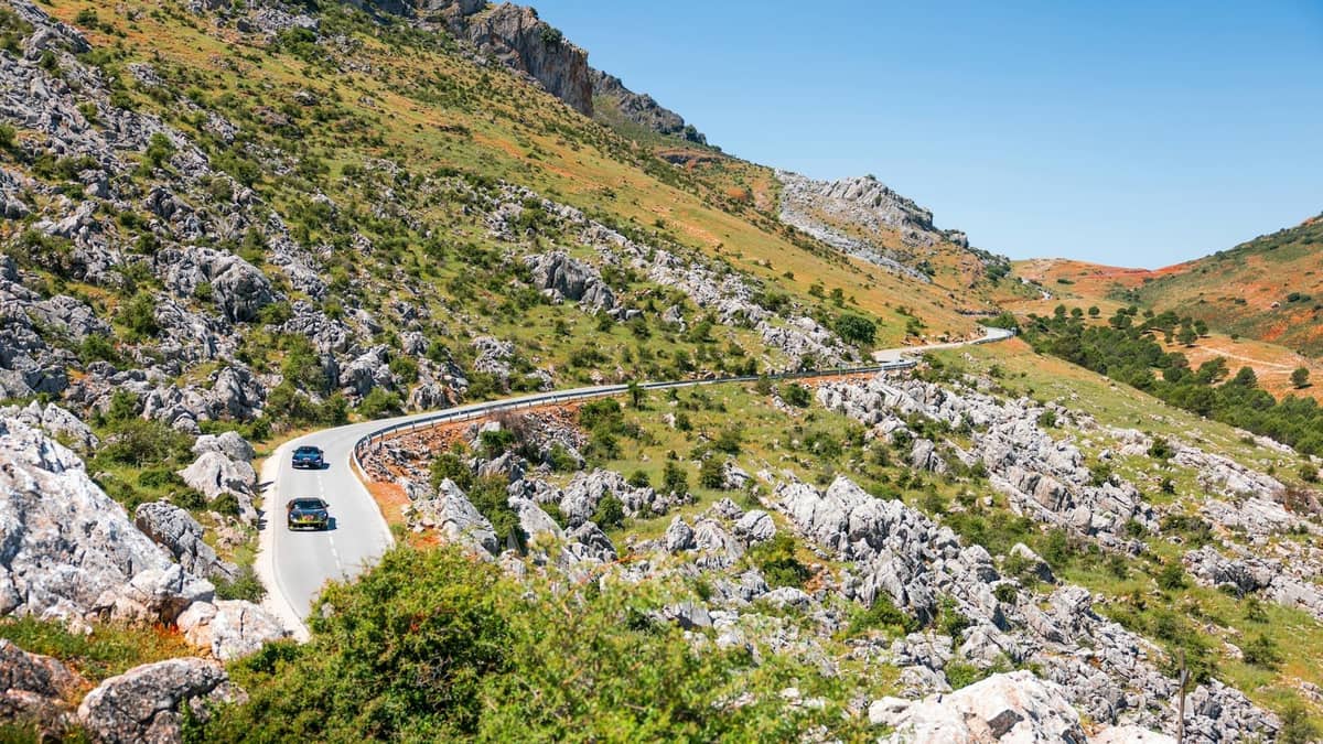 Strada di montagna tortuosa con auto che percorrono un terreno roccioso sotto un cielo azzurro limpido, tipica delle condizioni stradali rurali di Creta.