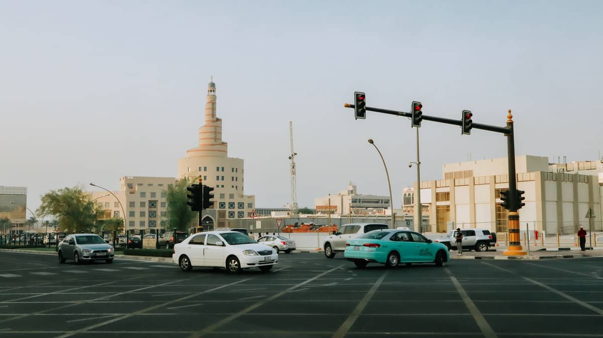 Belebte Kreuzung in Doha mit einem türkisfarbenen Karwa-Taxi, lokalem Verkehr und dem spiralförmigen Fanar Islamic Cultural Center im Hintergrund.