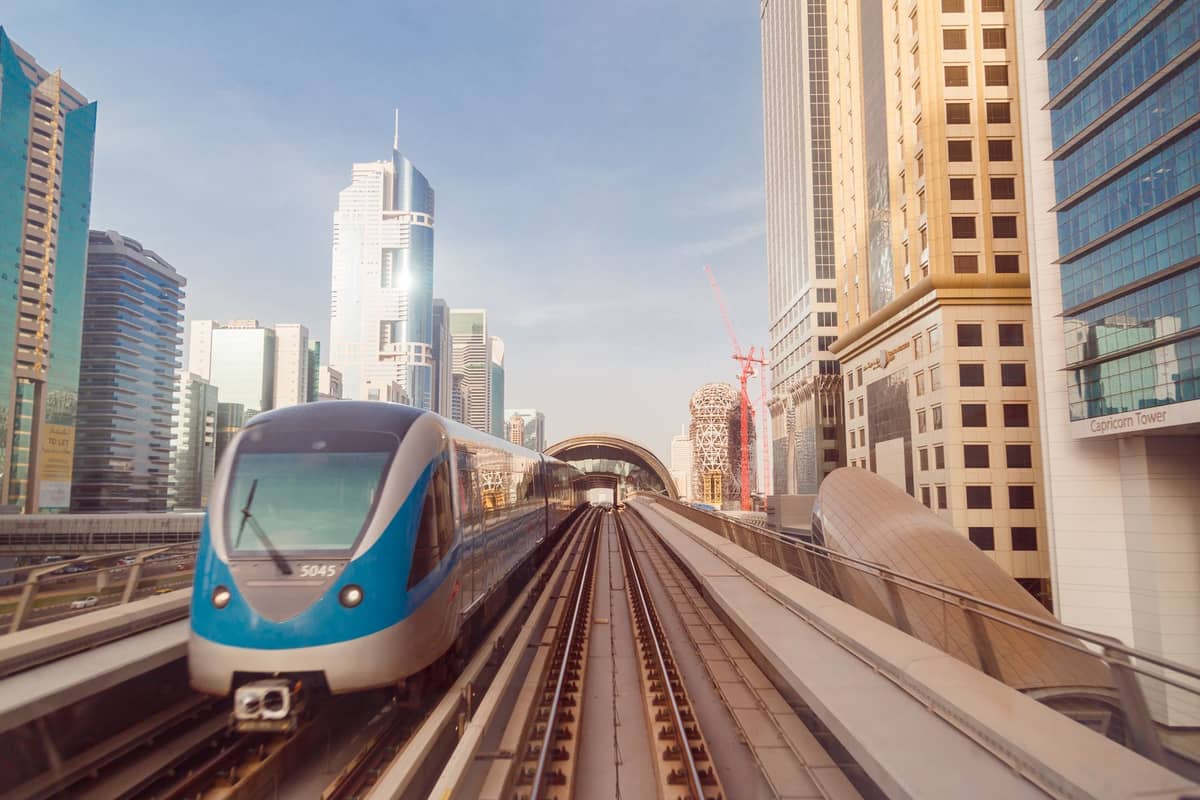Ein Zug der Dubai Metro nähert sich auf Hochgleisen mit modernen Wolkenkratzern im Hintergrund unter einem klaren Himmel.