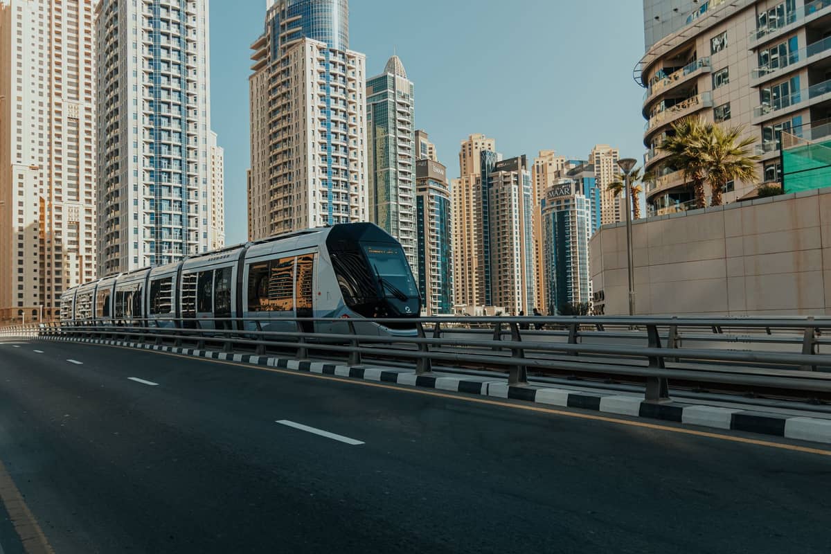 Die Dubai Tram fährt entlang einer Stadtstraße, umgeben von modernen Hochhäusern in Dubai Marina am Tag.