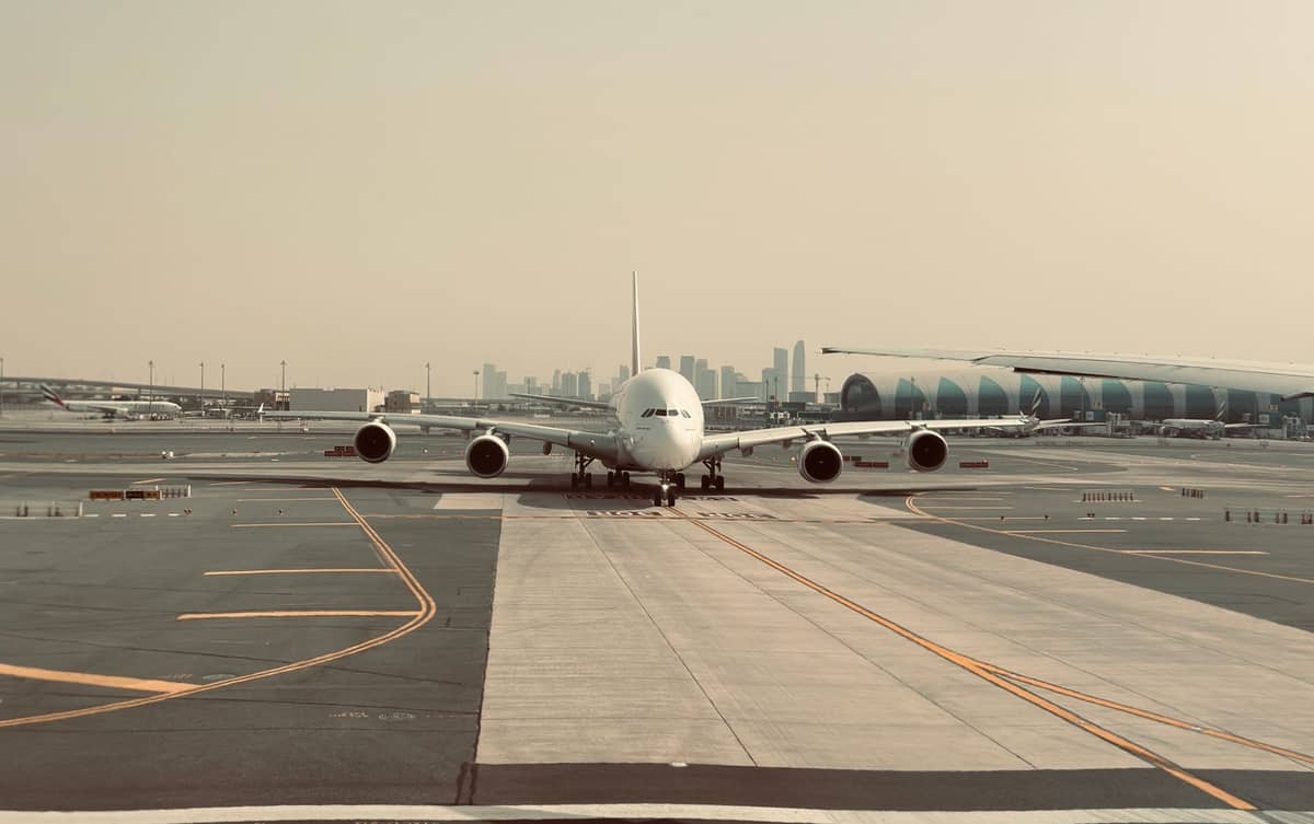 Ein Emirates A380 auf dem Rollfeld des Dubai International Airport, mit Terminalgebäuden und der Skyline von Dubai im Hintergrund.