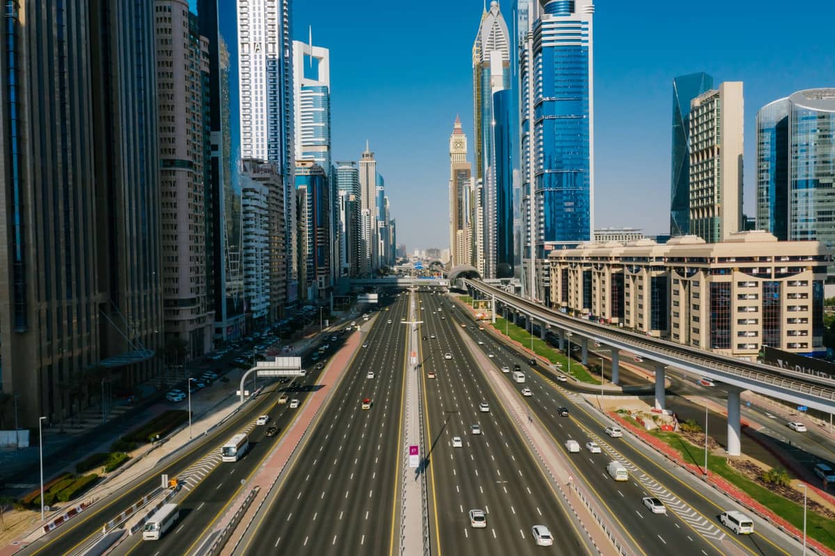 Weitwinkelansicht der Sheikh Zayed Road in Dubai mit Metroschienen, Hochhäusern und mehreren Fahrspuren unter einem klaren blauen Himmel.