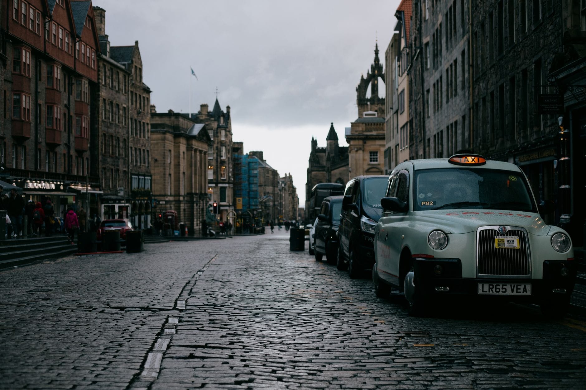 Eine Reihe schwarzer Taxis, die auf einer Kopfsteinpflasterstraße geparkt sind, mit historischen Gebäuden von Edinburgh im Hintergrund.