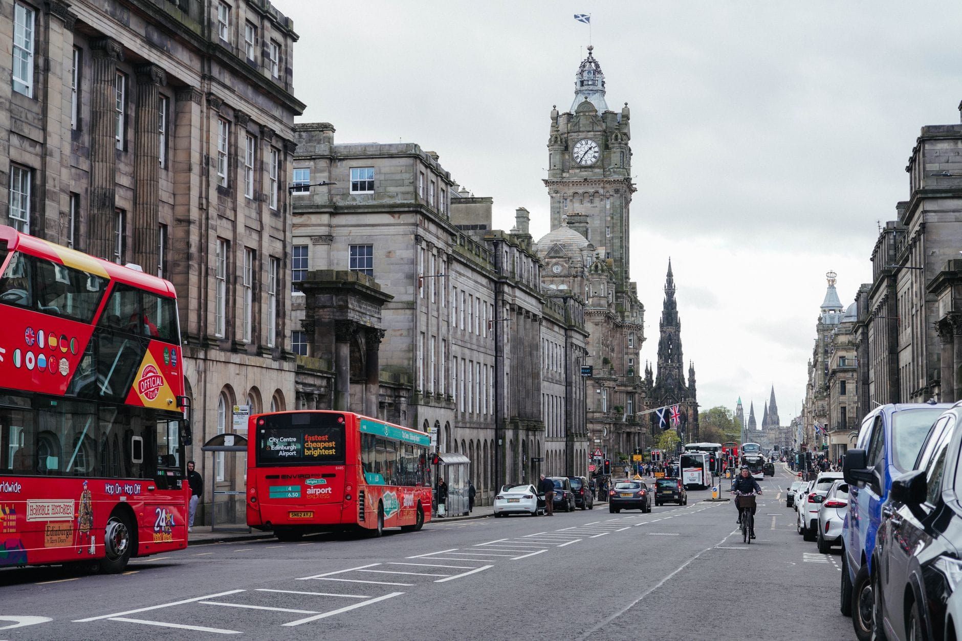 Blick auf die Princes Street in Edinburgh mit Lothian-Doppeldeckerbussen, Taxis, Radfahrern und historischen Gebäuden mit dem Uhrenturm des Balmoral Hotels.