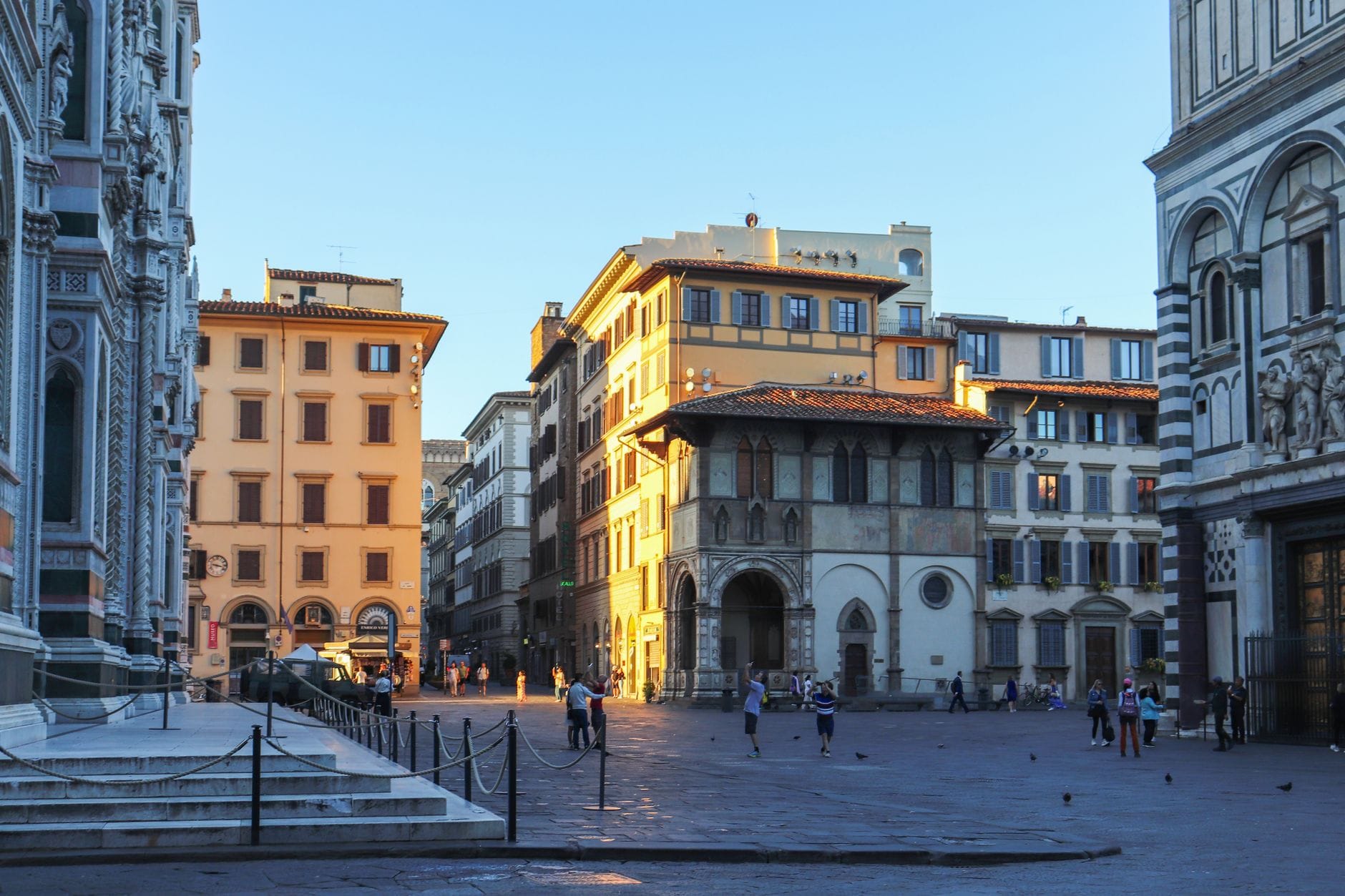 ปิอาซซ่าในเมืองฟลอเรนซ์ที่มีอาคารประวัติศาสตร์ เห็นส่วนหนึ่งของ Duomo และ Baptistery ผู้คนเดินเล่นและสนุกสนานในใจกลางเมืองใต้ท้องฟ้าสีฟ้าใส