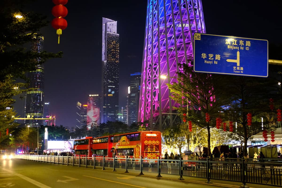 Double-decker bus near lit Canton Tower and street signs in central Guangzhou at night