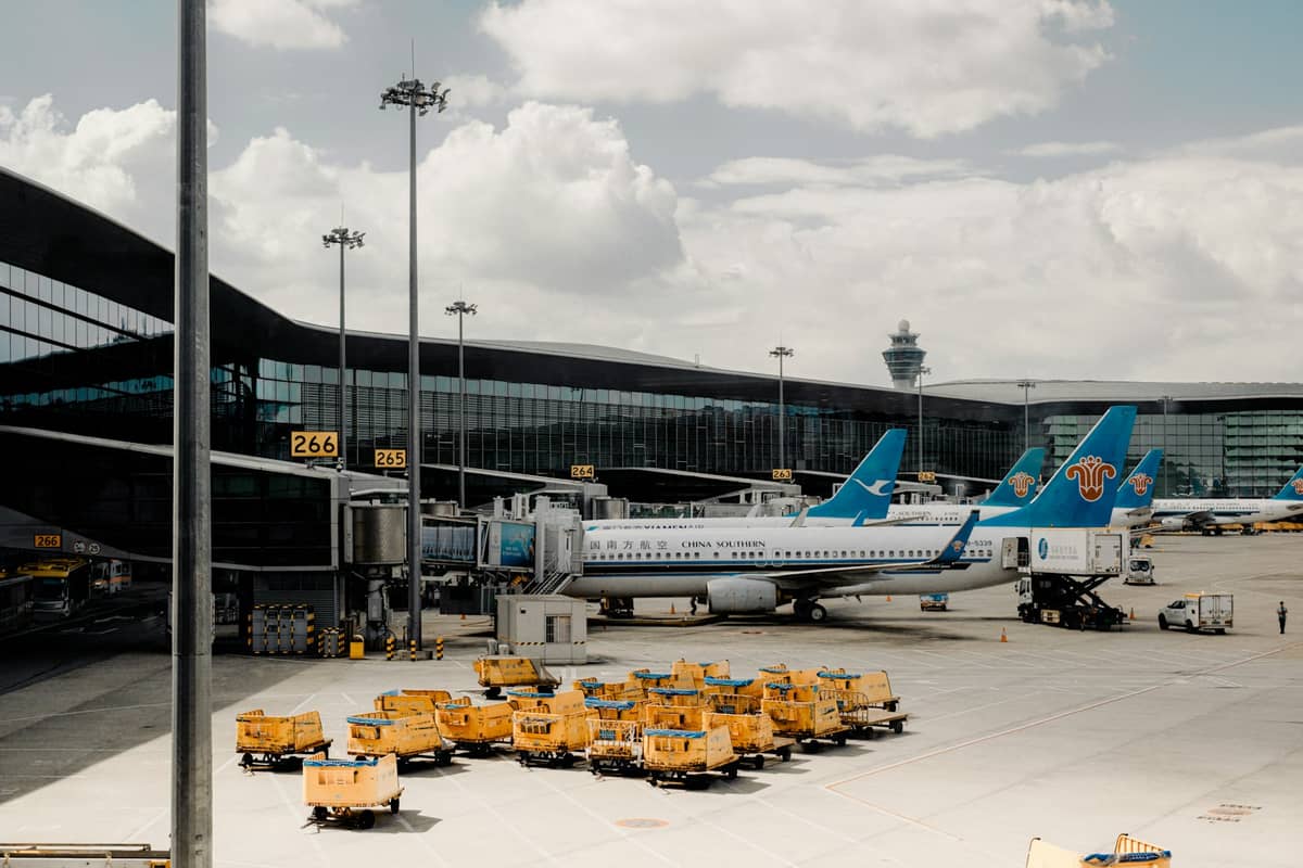 Modern airport terminal at Guangzhou Baiyun International Airport with China Southern Airlines planes parked at the gate and airport equipment visible on the tarmac.
