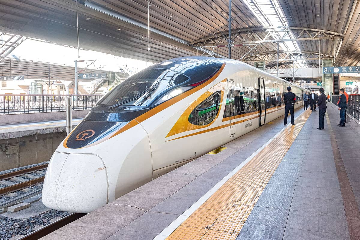 Modern Chinese high-speed train at a large city station platform with passengers and officers standing nearby under a glass roof.