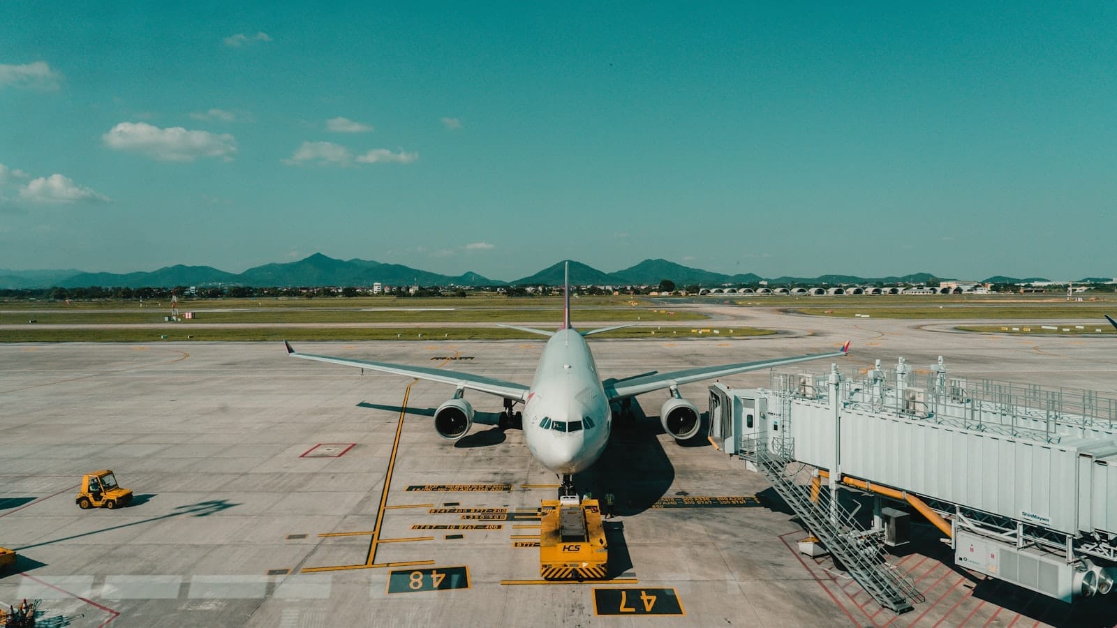 Aircraft parked at Noi Bai International Airport with jet bridge and runway visible under a blue sky.