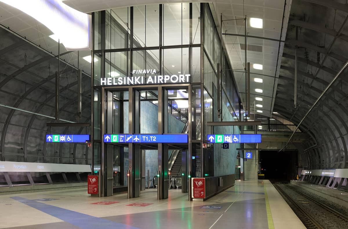 Vista da plataforma da estação de trem do Aeroporto de Helsinki com sinalização clara para os terminais do aeroporto e acesso ferroviário.