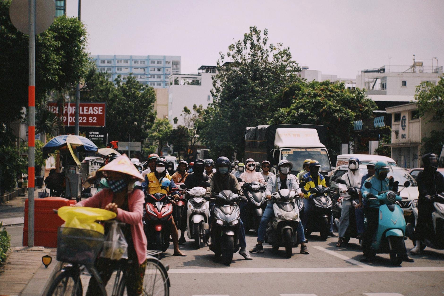 Ngã tư tấp nập tại Thành phố Hồ Chí Minh với nhiều xe máy và một người đạp xe ở phía trước tại vạch sang đường.