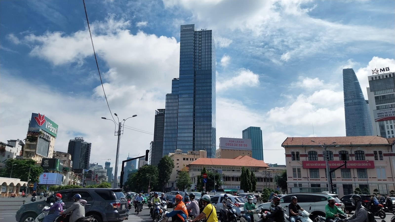 Escena callejera de Ciudad Ho Chi Minh con intenso tráfico de motos y autos, rascacielos modernos y cielo azul, capturando el ambiente dinámico de la ciudad.