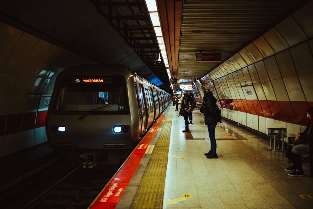 İstanbul metro istasyonunda peronfa durmuş tren, bekleyen yolcular ve yerde kırmızı hat işaretleri.
