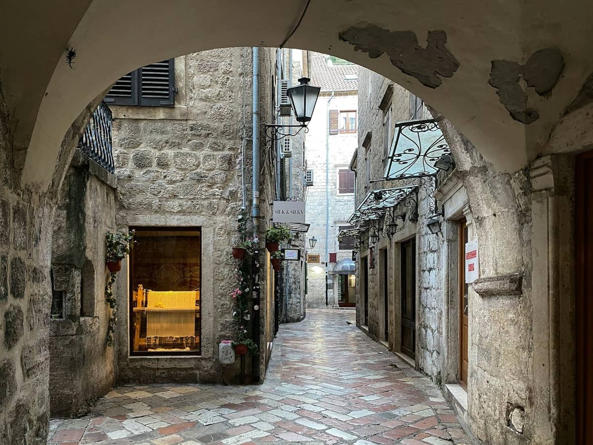 Narrow cobblestone alleyway lined with old stone buildings and archways in Kotor Old Town, Montenegro.