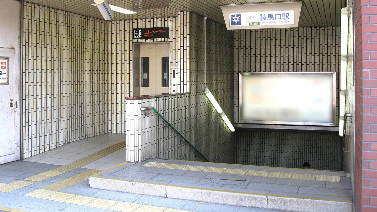Entrance and elevator of Kyoto's Karasuma subway line at Kuramaguchi Station, showing tactile paving and signage.