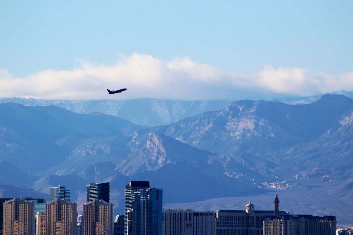 Avión despegando sobre el skyline de Las Vegas con hoteles del Strip y montañas al fondo bajo un cielo despejado.