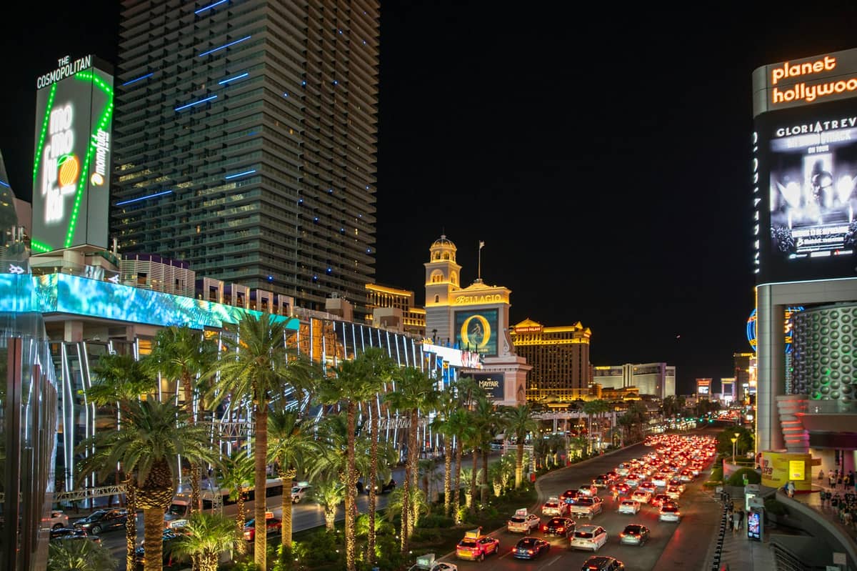 Vista nocturna del Strip de Las Vegas con Planet Hollywood, palmeras, tráfico, peatones y hoteles-casino iluminados a lo largo del bulevar.