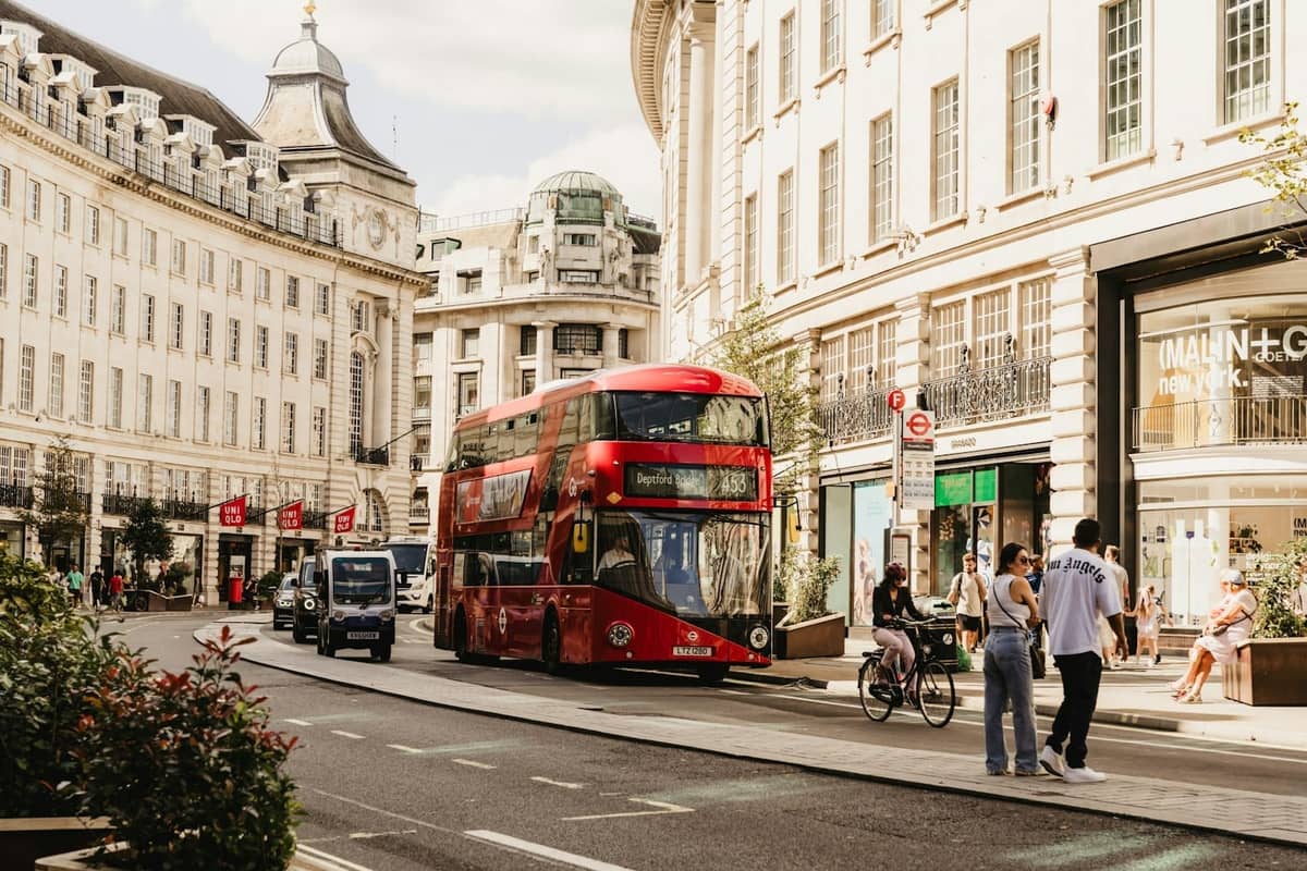 Um clássico ônibus vermelho de dois andares de Londres percorre os icônicos edifícios curvos de Regent Street em um dia ensolarado, com pedestres e ciclistas nas proximidades.