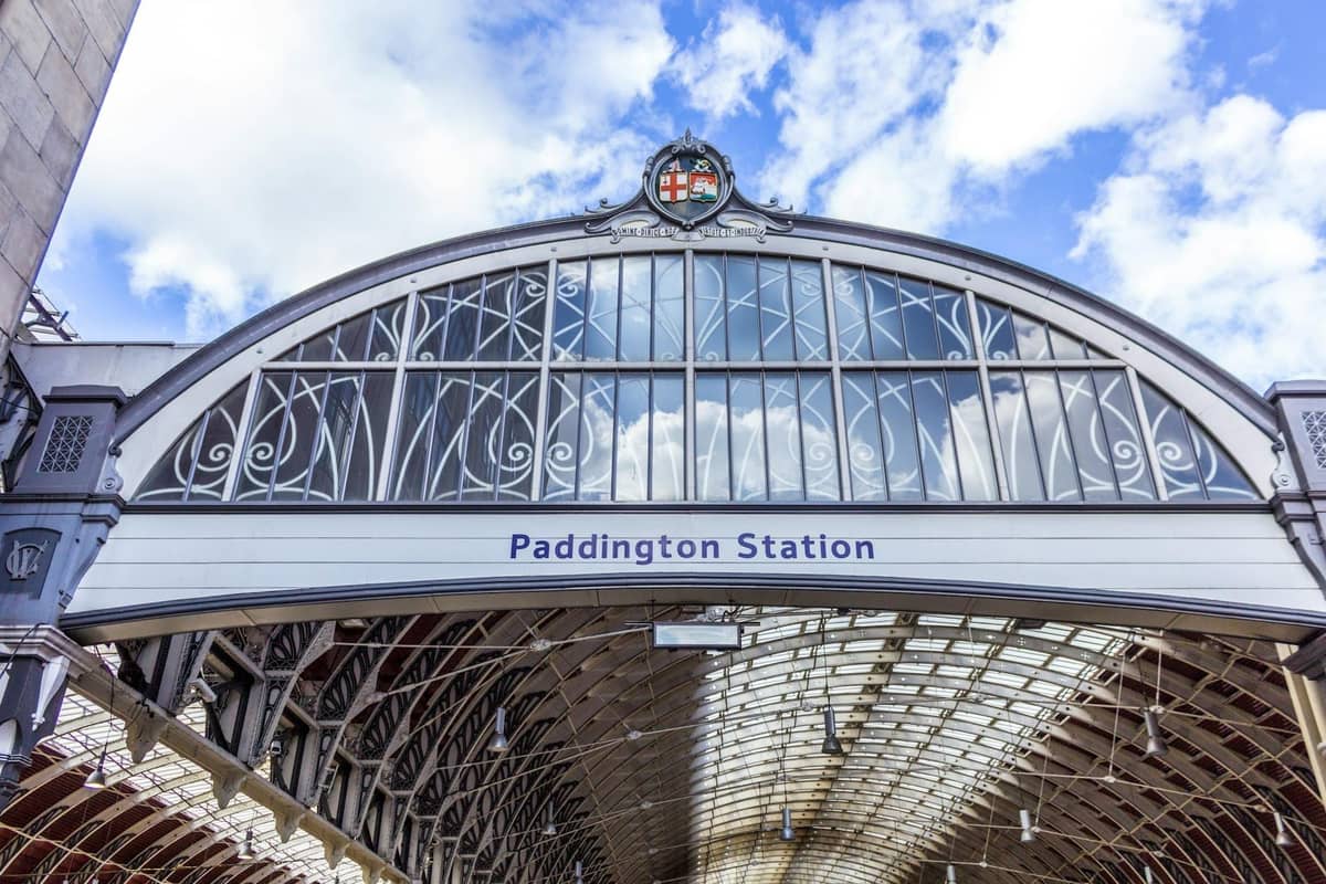 A entrada exterior da London Paddington Station com a sua placa e telhado de vidro arqueado num dia luminoso com céu azul e nuvens.