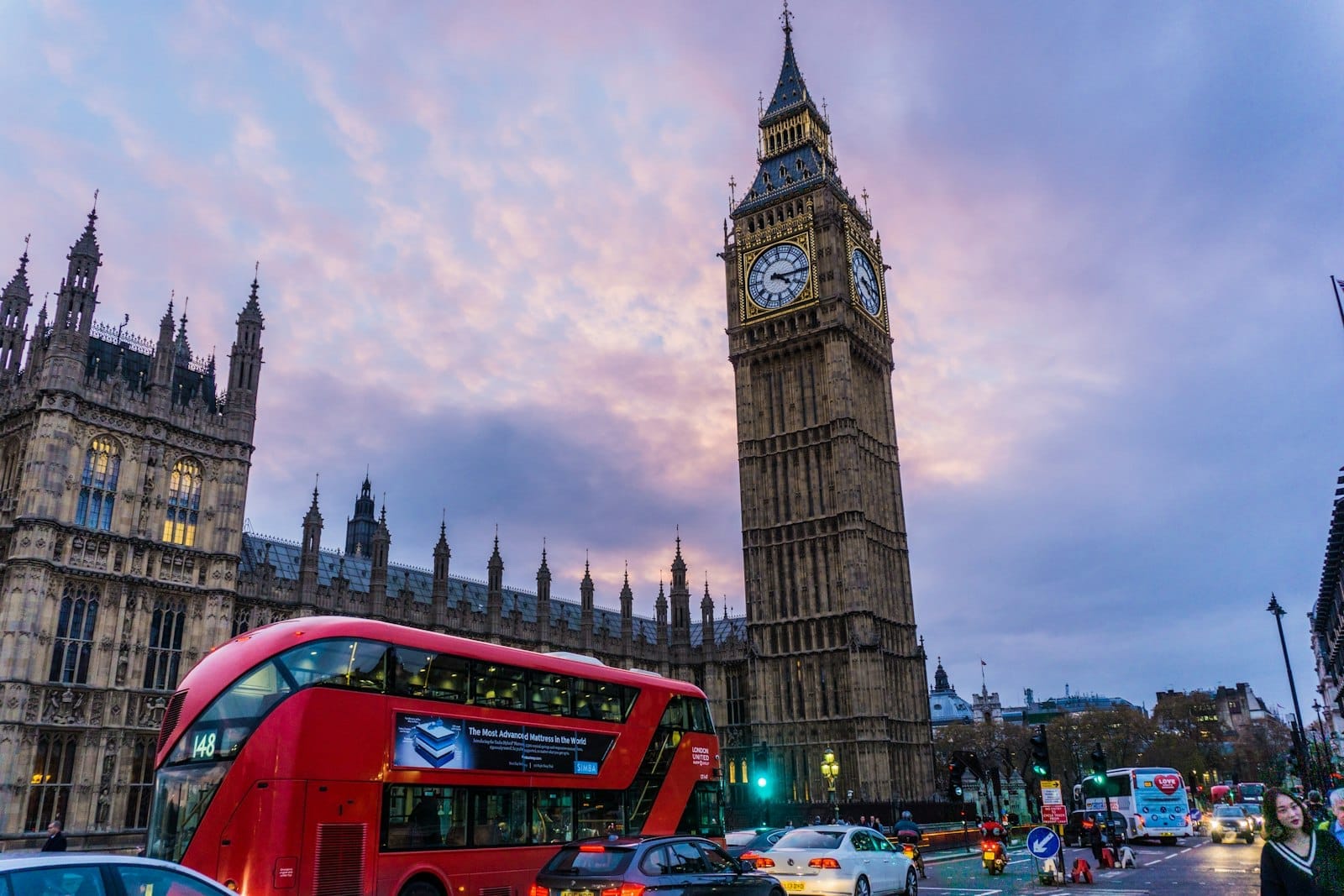 O icônico ônibus double-decker de Londres e o trânsito movimentado em frente ao Big Ben ao pôr do sol, com um céu colorido e atmosfera clássica da cidade.