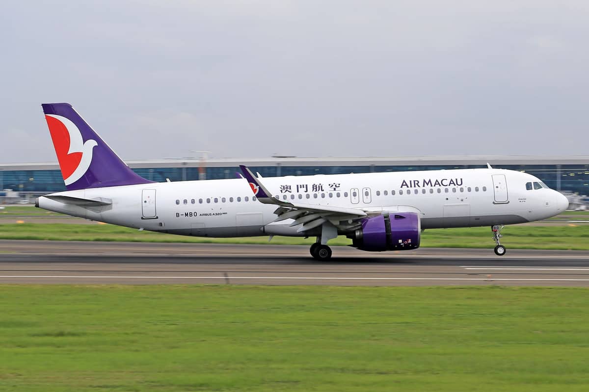 Ein Flugzeug von Air Macau auf der Startbahn mit dem Flughafenterminal im Hintergrund an einem bewölkten Tag.